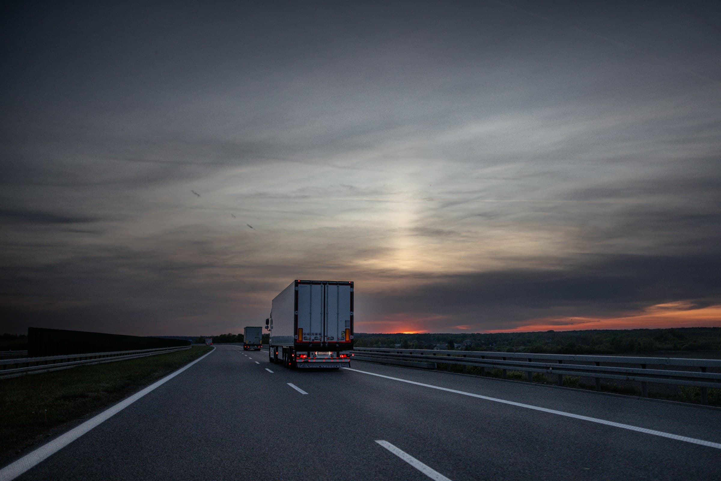 A tractor-trailer travelling a multi-lane highway toward the horizon at dusk.